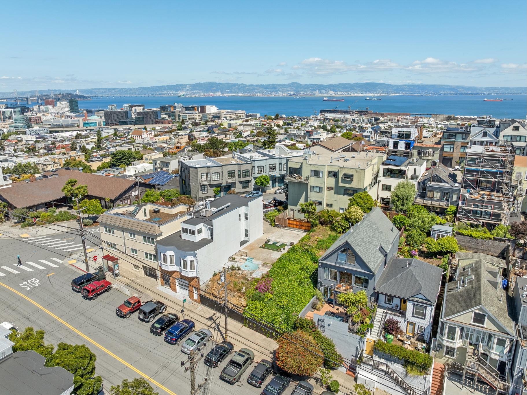 Aerial view of a city with residential houses, taller buildings, a body of water, and ships in the distance on a sunny day.