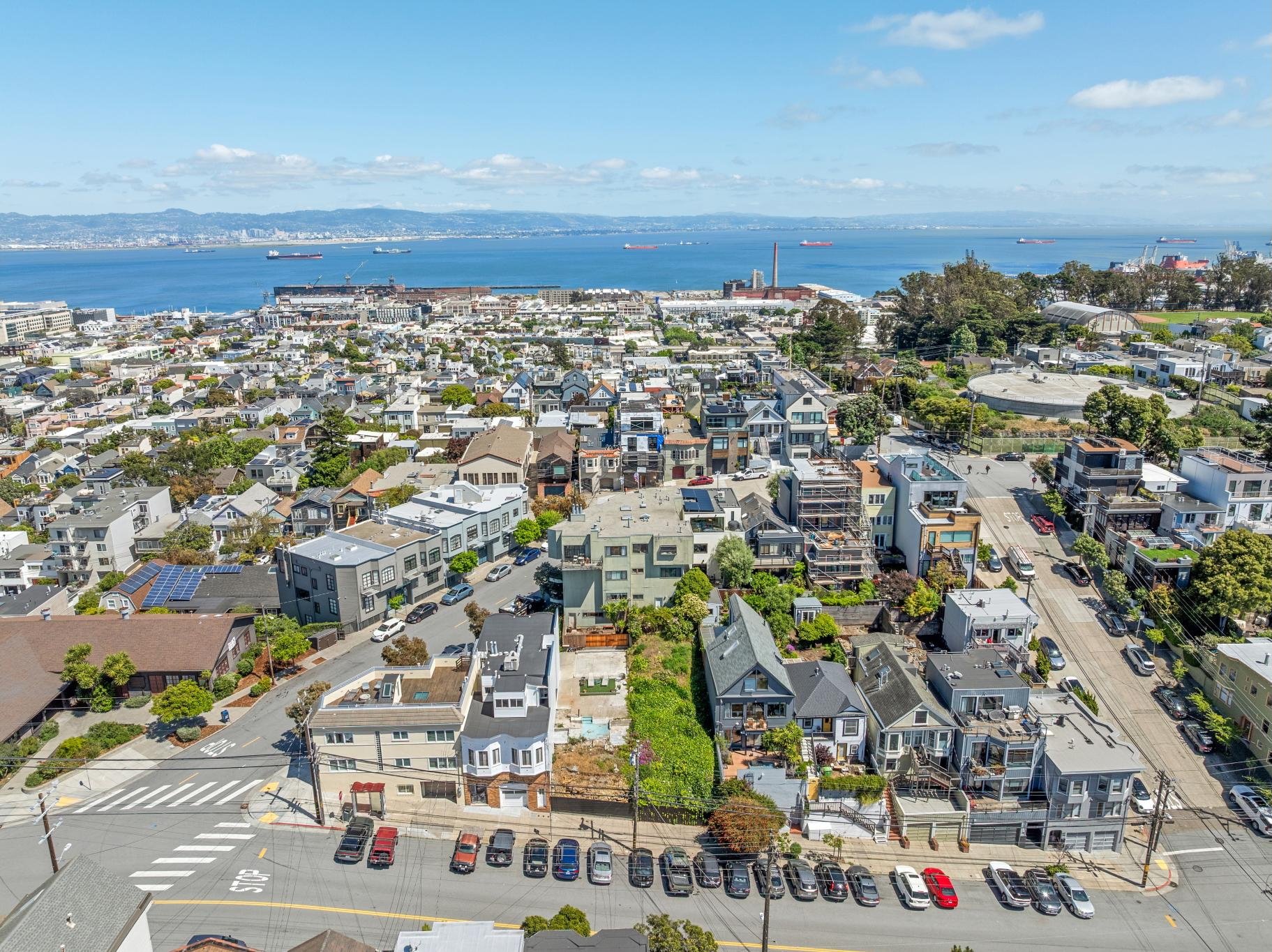 View of a coastal city with a large body of water and ships in the background. Residential buildings and streets in the foreground.