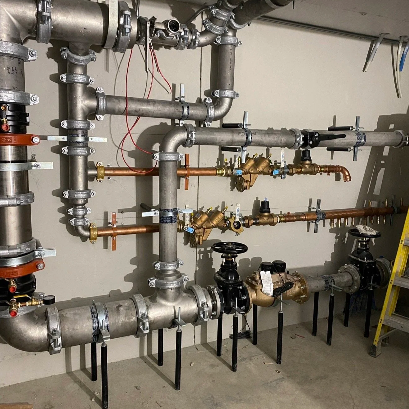 A complex plumbing system with multiple pipes, valves, and fittings attached to a wall in a building's utility room.