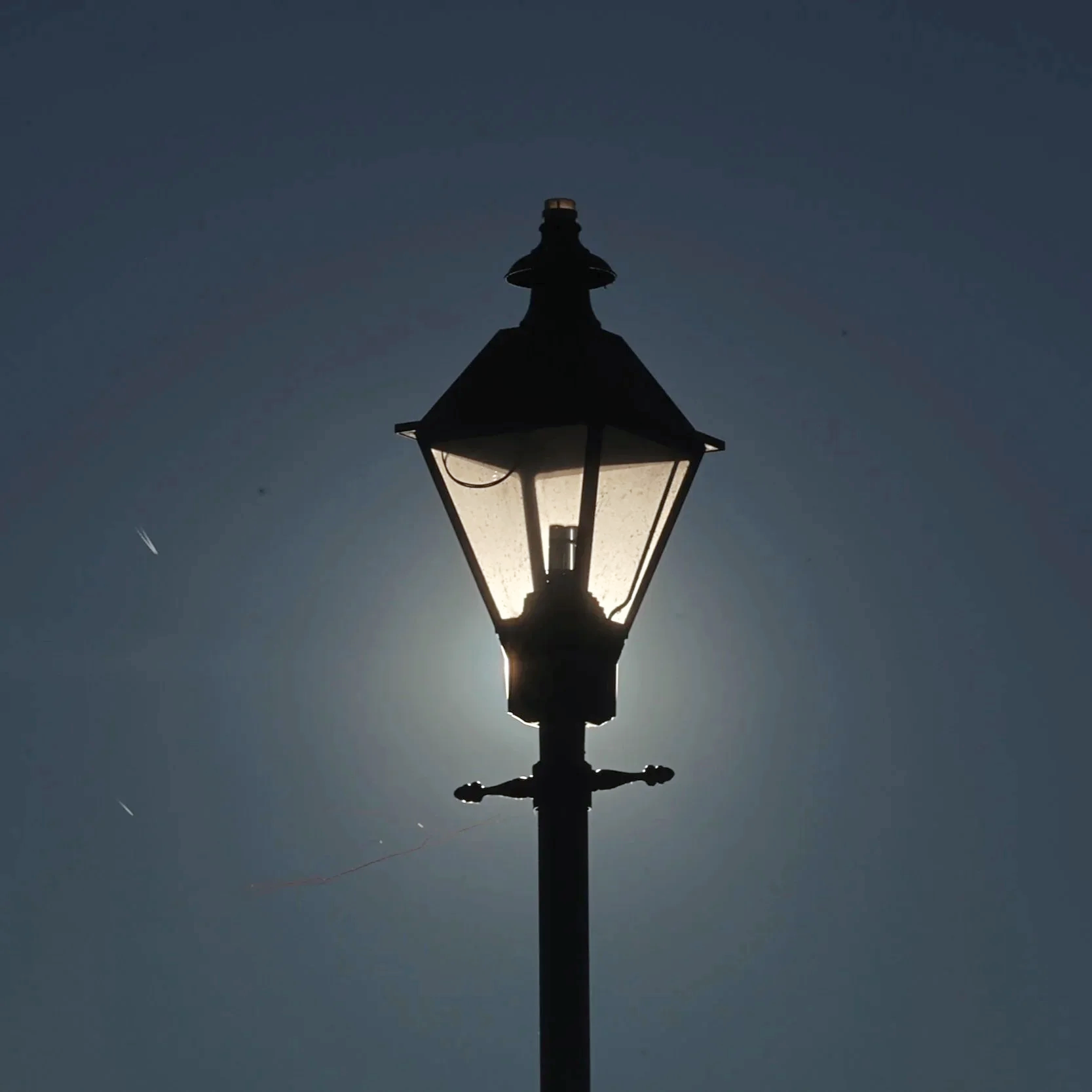 A streetlamp silhouette with a bright light inside against a dark evening sky