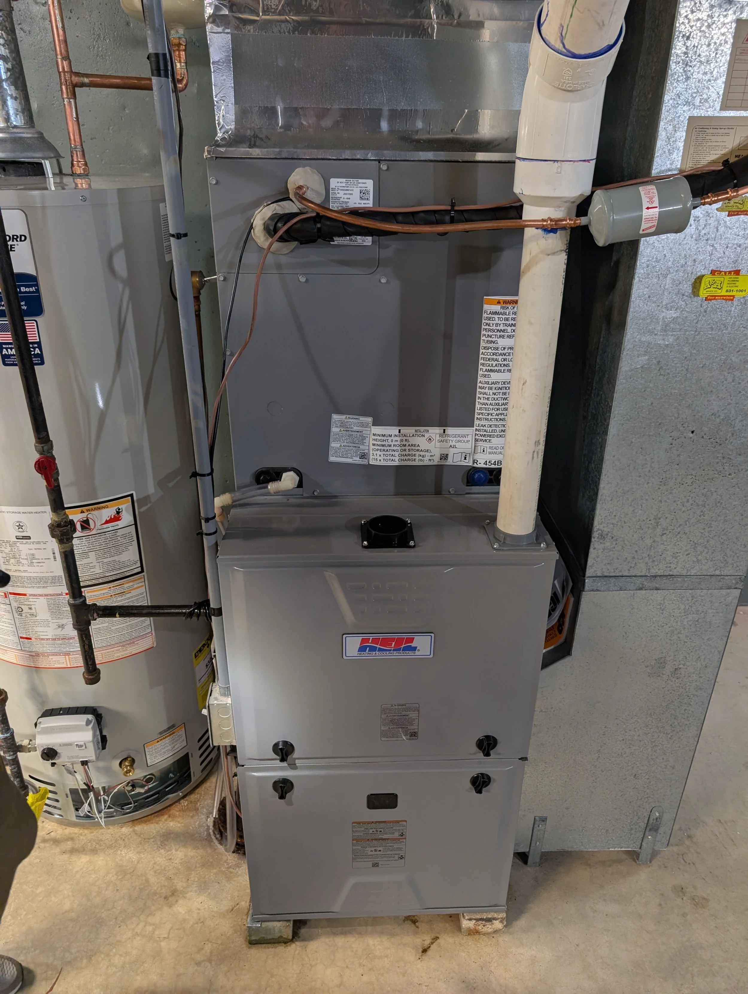 A furnace or HVAC unit installed in a basement or utility room with exposed copper and PVC pipes, and related mechanical components.