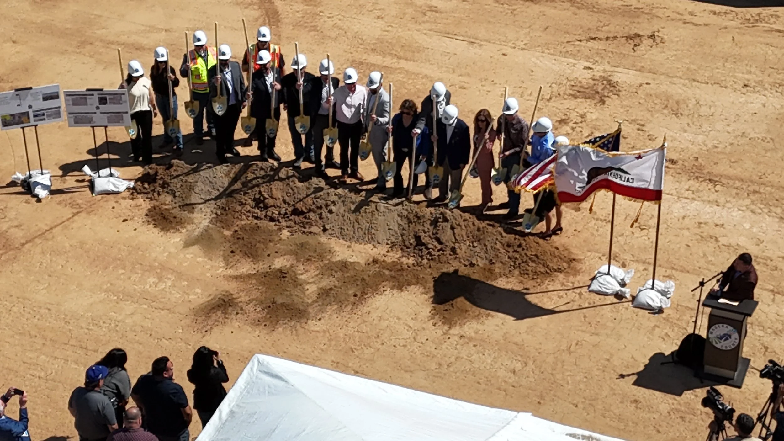 All groundbreaking participants lifting up their golden shovels smiling for pictures wearing their white hard hats. 