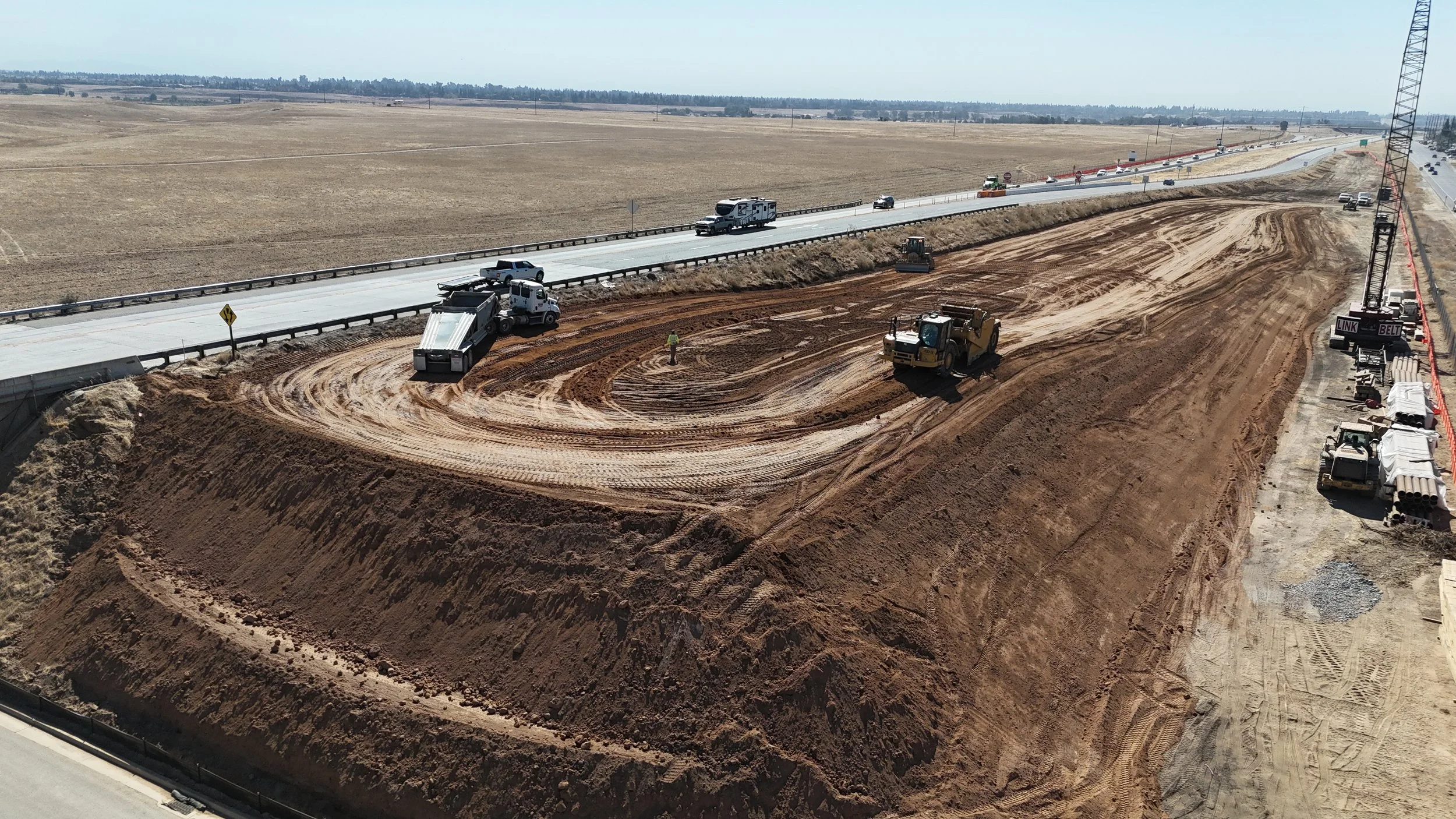 A large mound of dirt being compacted on the right of the Avenue 11 bridge.