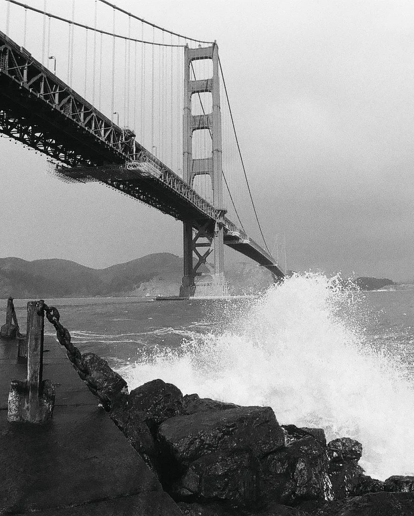 The golden gate bridge at fort point in san francisco, ca.  Waves crashing over rocks. Film photography