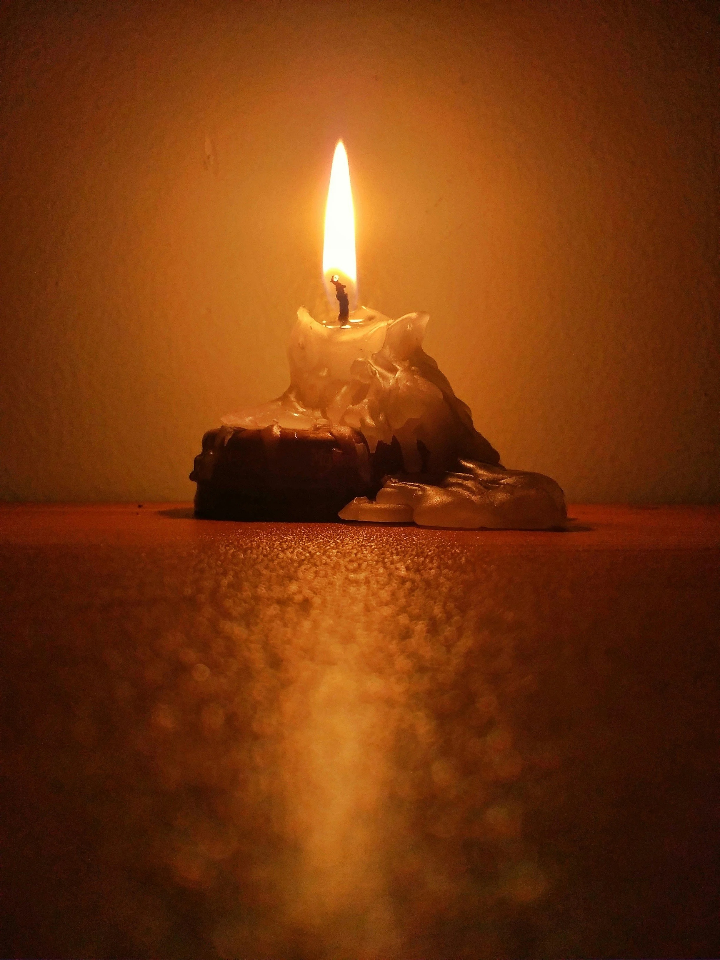 A lit candle with melting wax on a dark background, casting a warm glow.