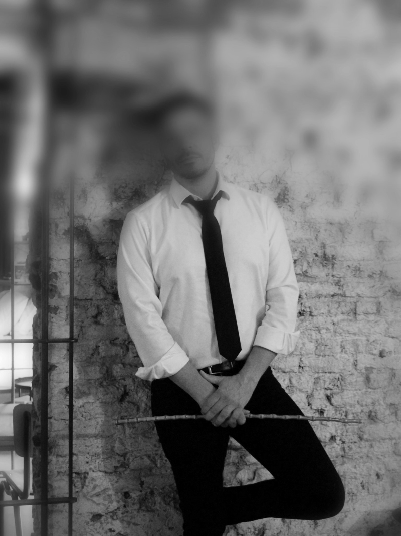 BDSM Gigolo, foto van een man met een overhemd en zwarte stropdas en een stok in zijn handen
