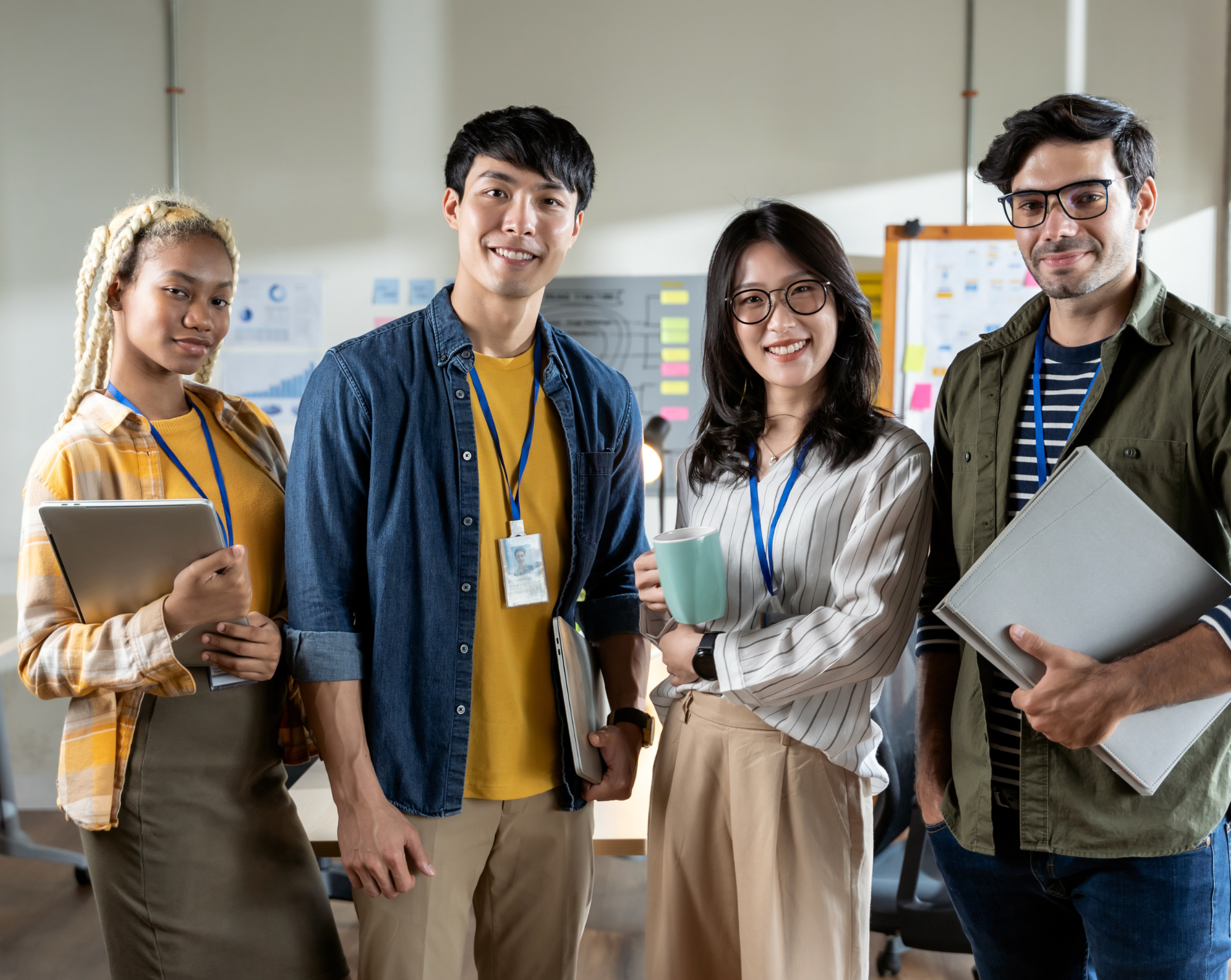 Group of four diverse professionals smiling in an office with charts and notes on the walls.