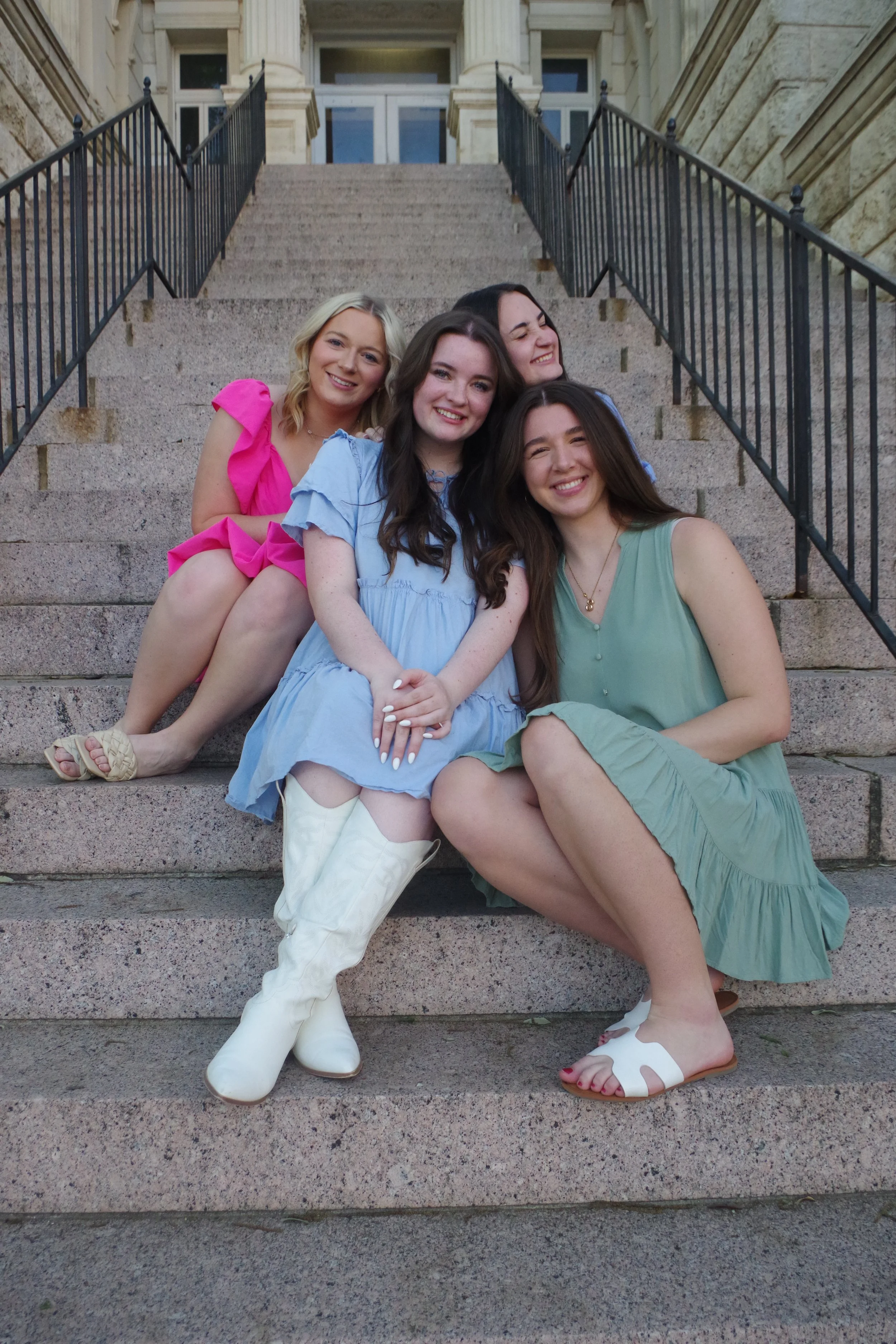 Five young women sitting on stone steps in front of a building, smiling and posing for the photo.