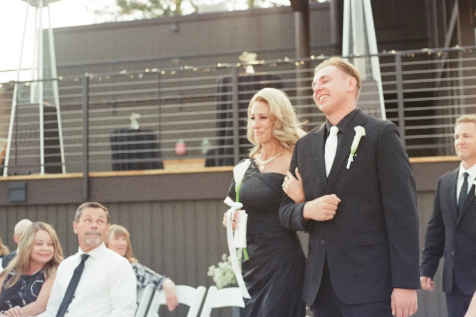 A groom walking a bride down the aisle during a wedding ceremony with guests watching.