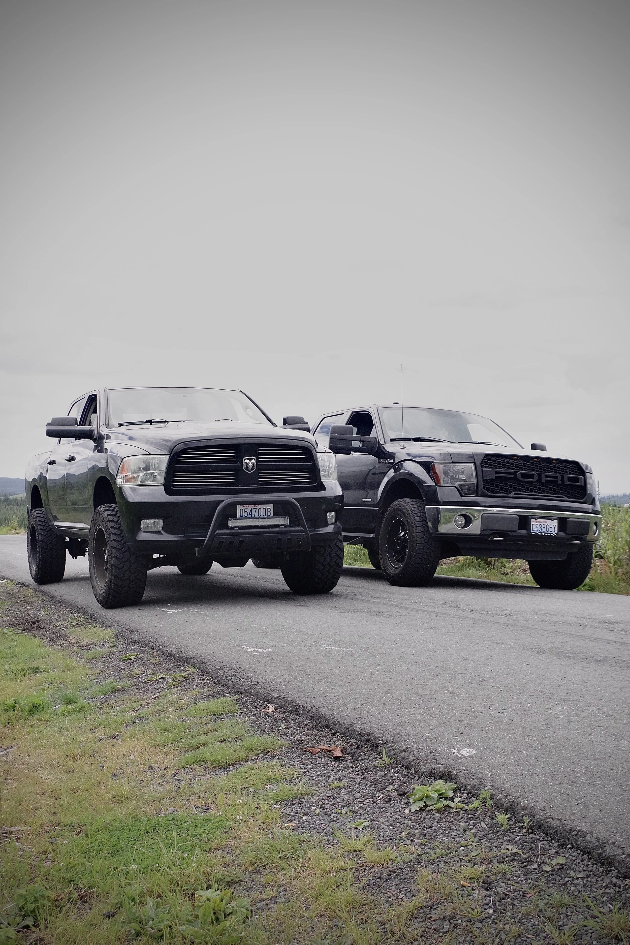 Two black pickup trucks parked on a rural road, one Ram and one Ford.