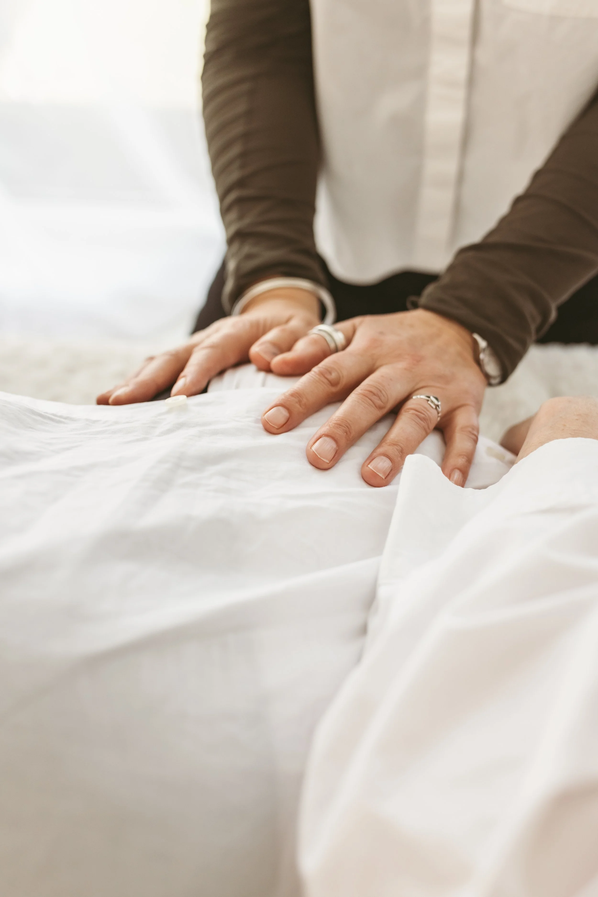 A person wearing a dark long-sleeve shirt pressing down on a white sheet with their hands, which have rings on the fingers.