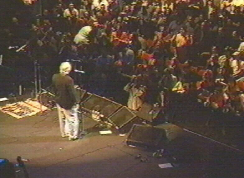 A man on stage with a microphone, facing a large audience in a dark theater.