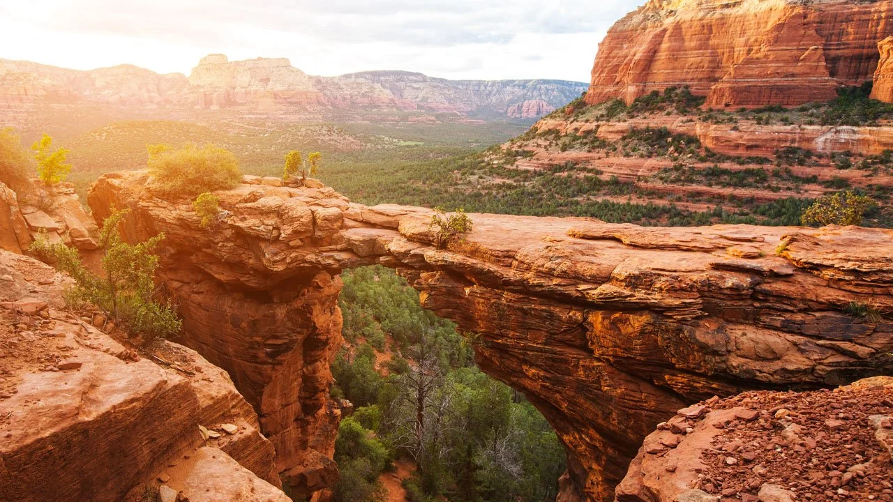 Sunset over red rock canyon with a natural rock bridge and green vegetation below