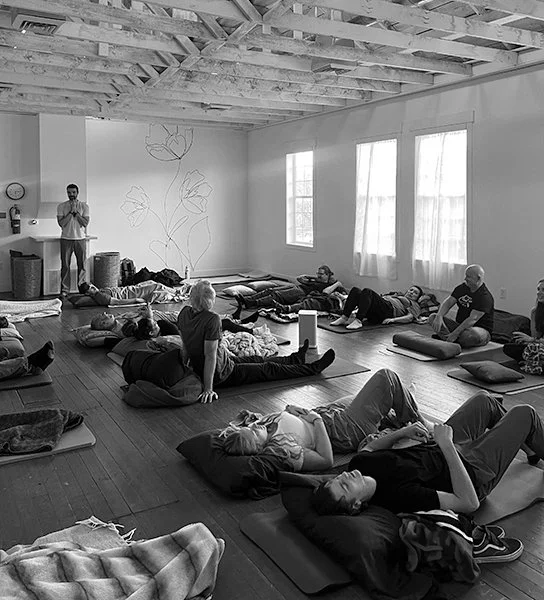 People meditating and practicing yoga in a spacious, well-lit room with wooden floors and exposed ceiling beams.