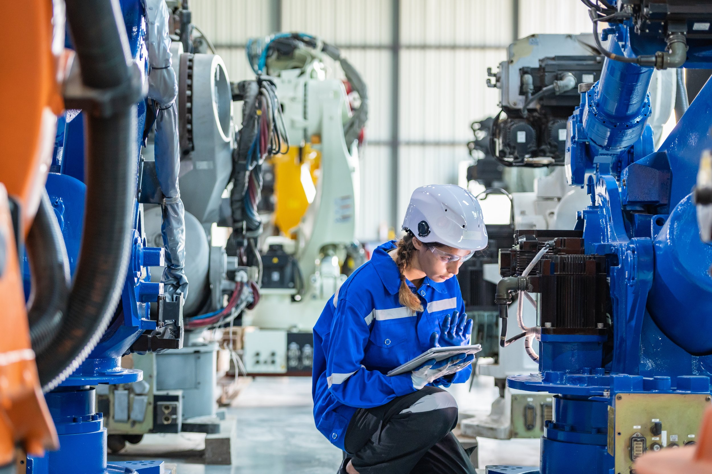 A female worker in safety gear working with industrial machinery in a factory or manufacturing plant.