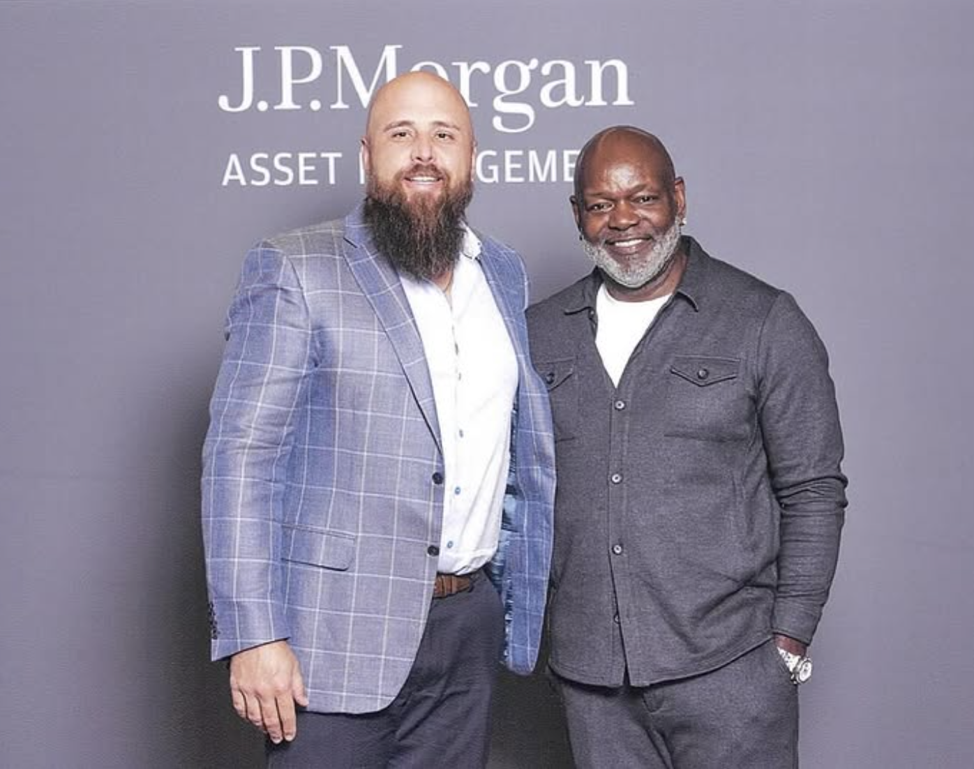 Two men standing together in front of a grey wall with J.P. Morgan Asset Management logo, smiling for the photo.