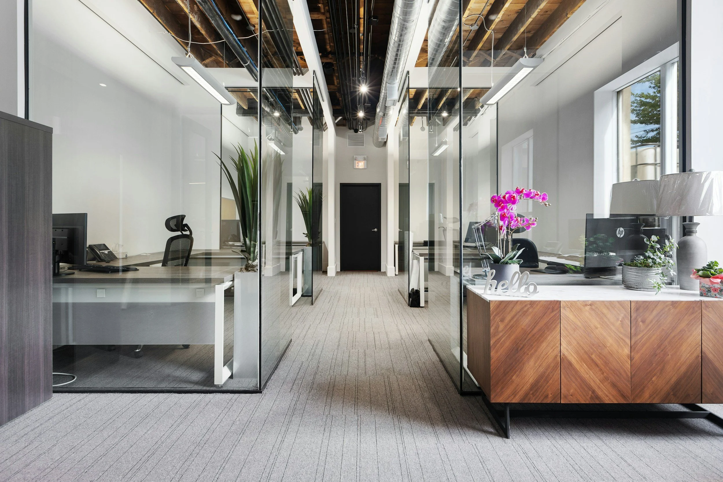 A modern office space with glass partitions, a reception desk with pink orchids, and visible ceiling ductwork and lighting fixtures.