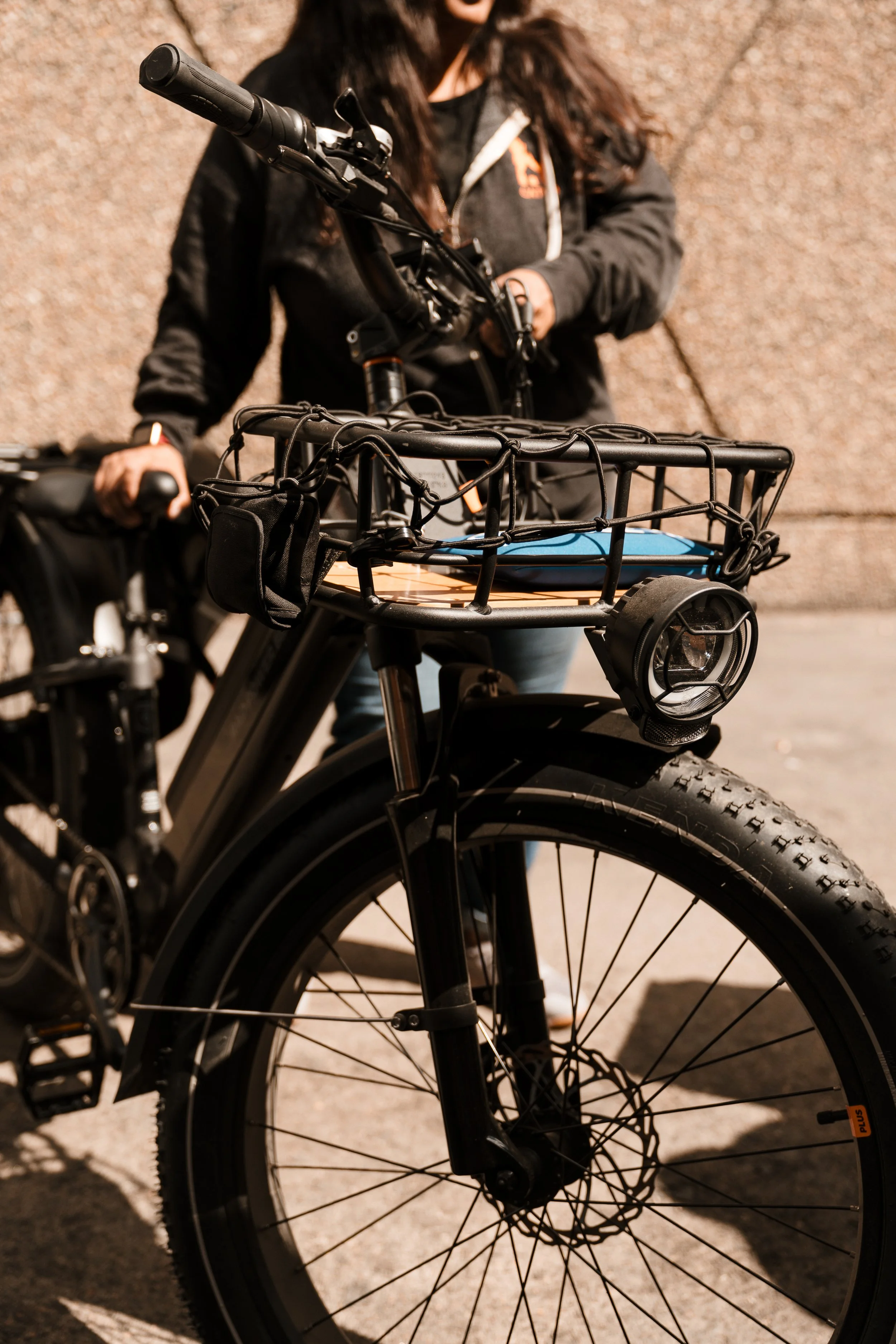 Close-up of a black electric bicycle with a front basket, parked outdoors on a concrete surface.