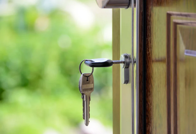 A close-up of a house door with a key inserted into the door lock, and a keyring with two keys hanging from it.