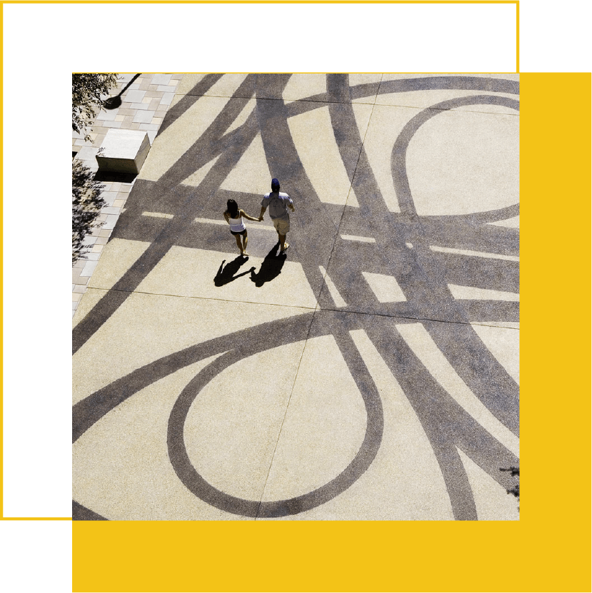 A couple walking hand in hand on sidewalk with large abstract shadow patterns.