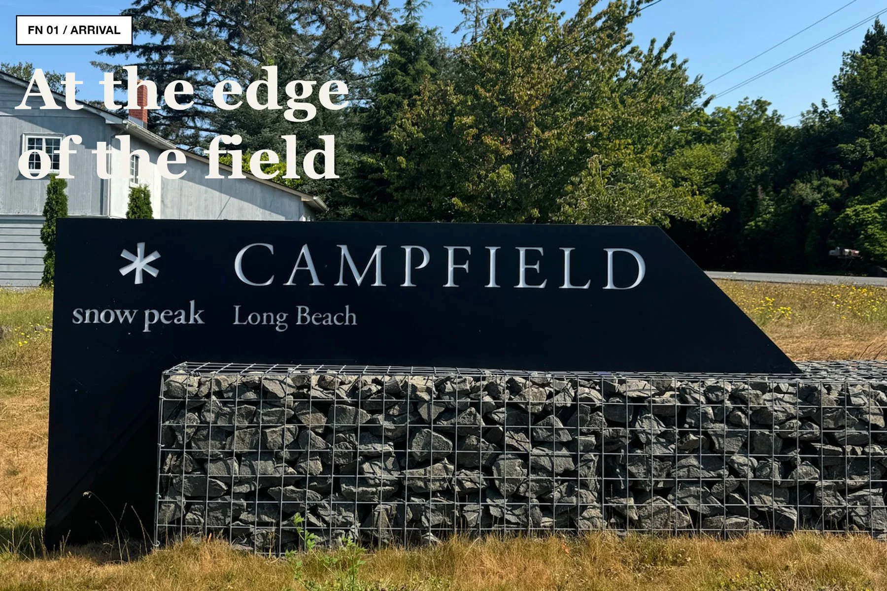 Snow Peak Campfield entrance sign for Long Beach, set in front of trees and a gabion stone wall.