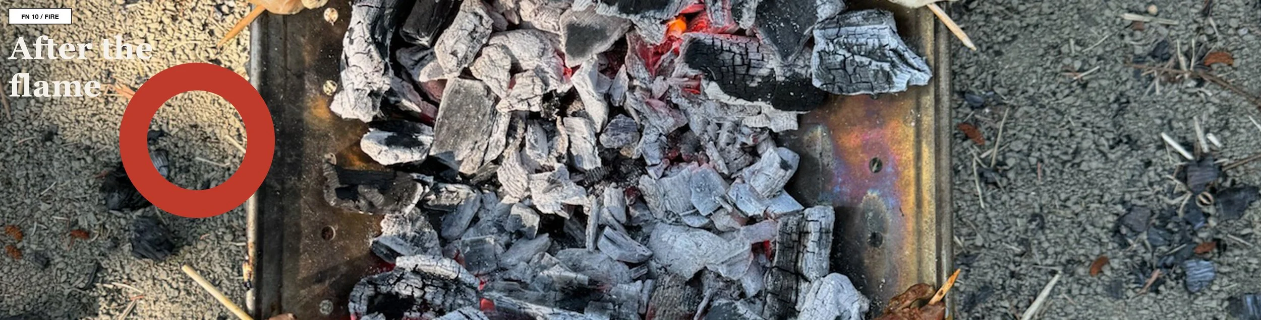 Overhead view of a circular campfire ring with ash, charred wood, and a concrete surround.