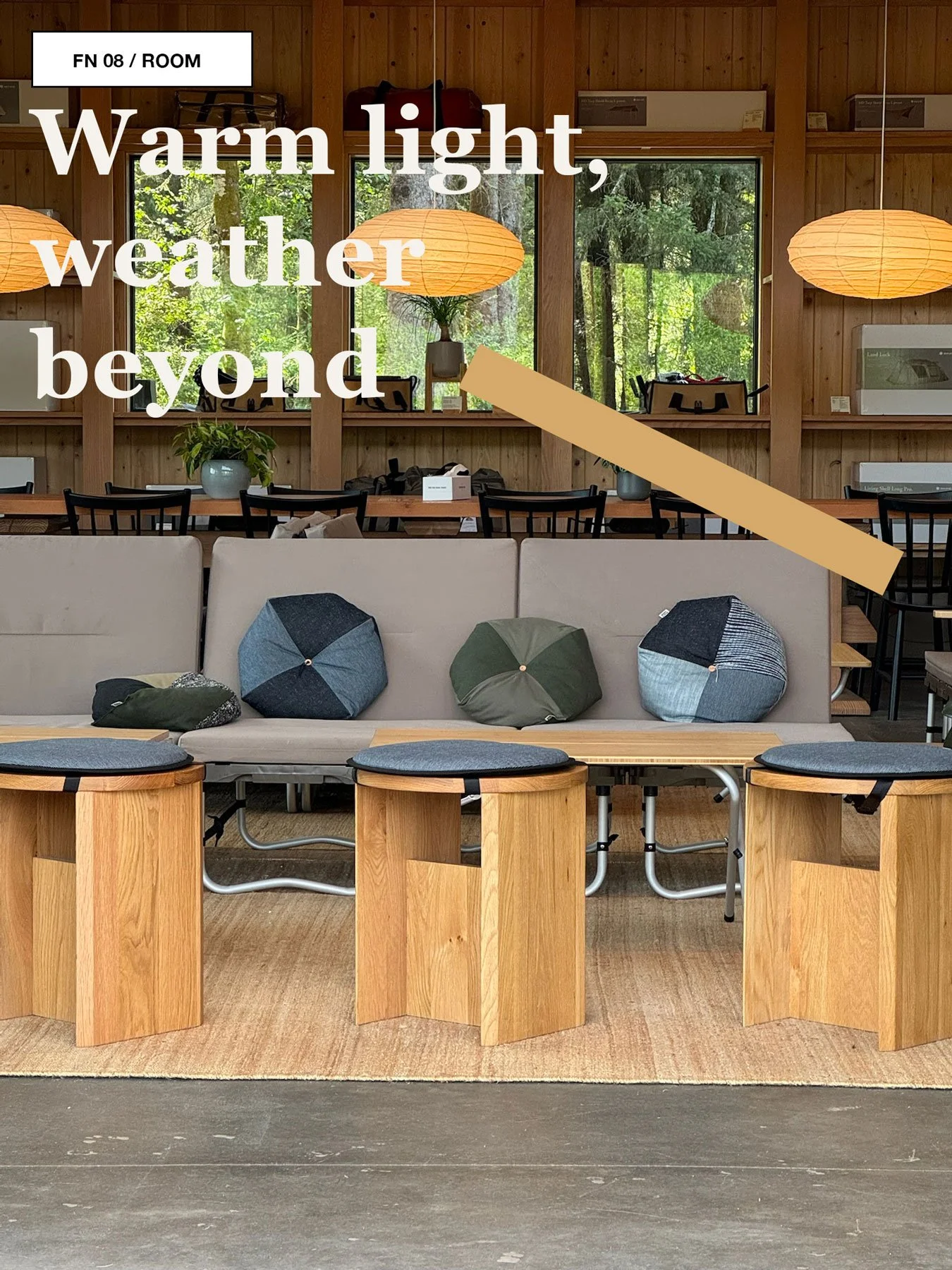 Communal lounge room at Snow Peak Campfield with warm pendant lights, tables, chairs, and large windows facing trees.
