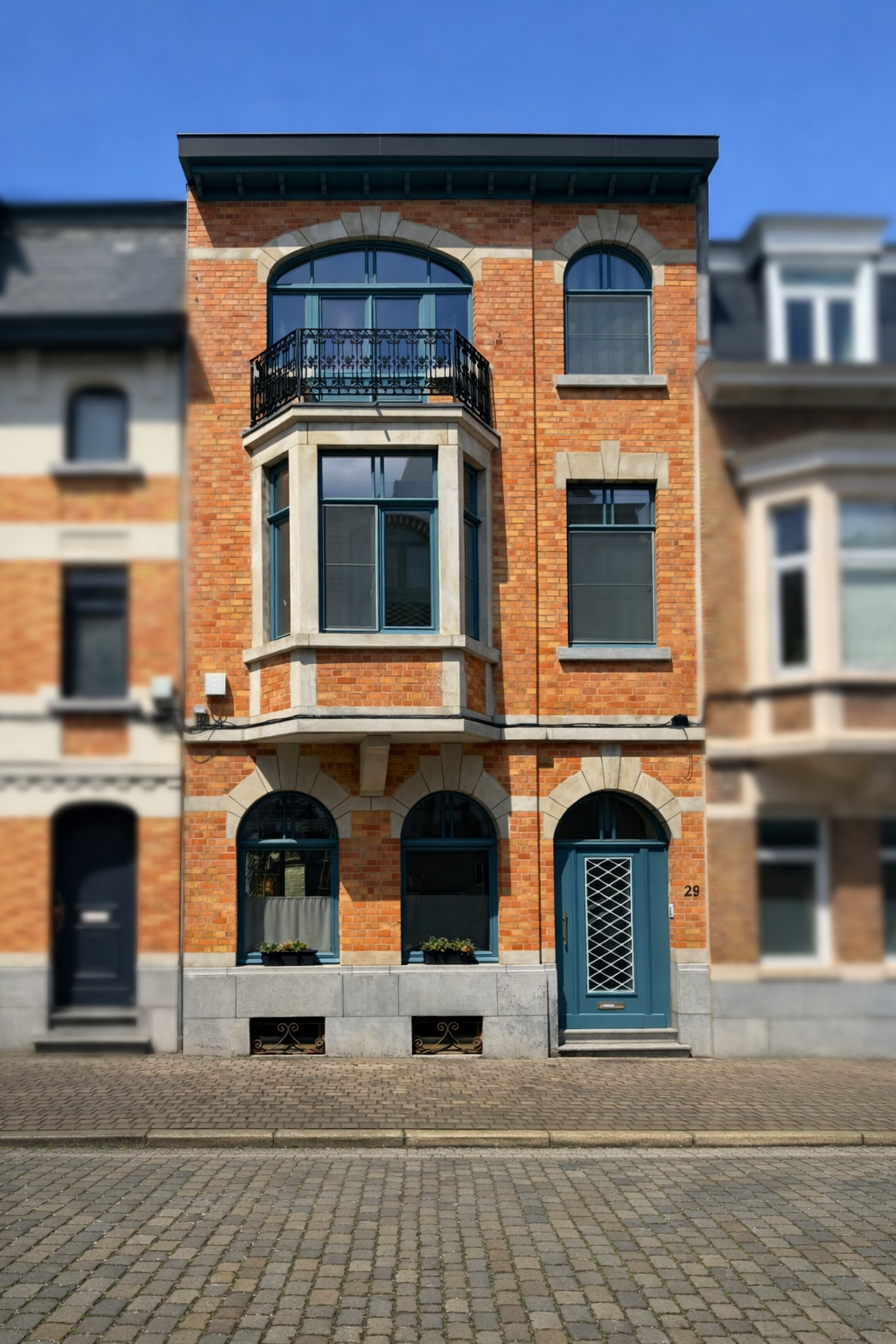 Three-story brick townhouse with arched and rectangular windows, blue front door with a lattice design, and small balcony with ornate black railing on the second floor. Attached neighboring townhouses visible on either side.