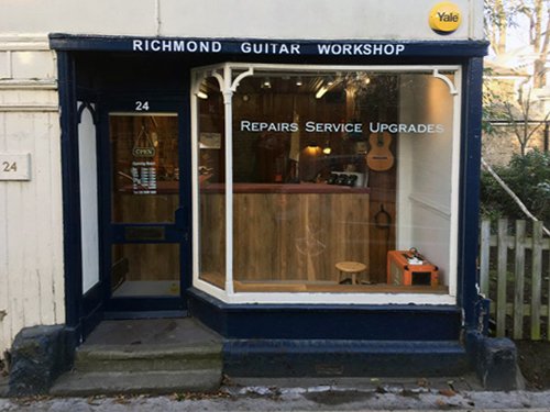 Front of Richmond Guitar Workshop with a door on the left and a large glass window displaying guitars inside. Sign above says 'Richmond Guitar Workshop' and the window has text 'Repairs Service Upgrades'.