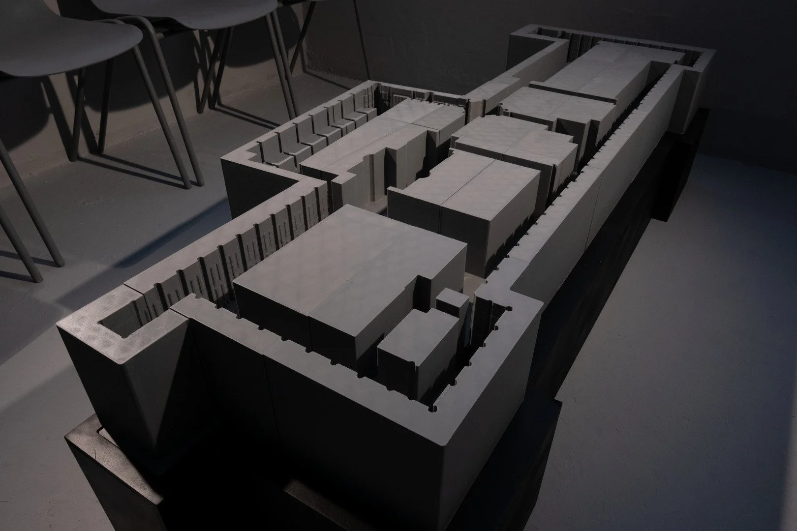 A detailed architectural model of a building layout on a table, with chairs nearby.