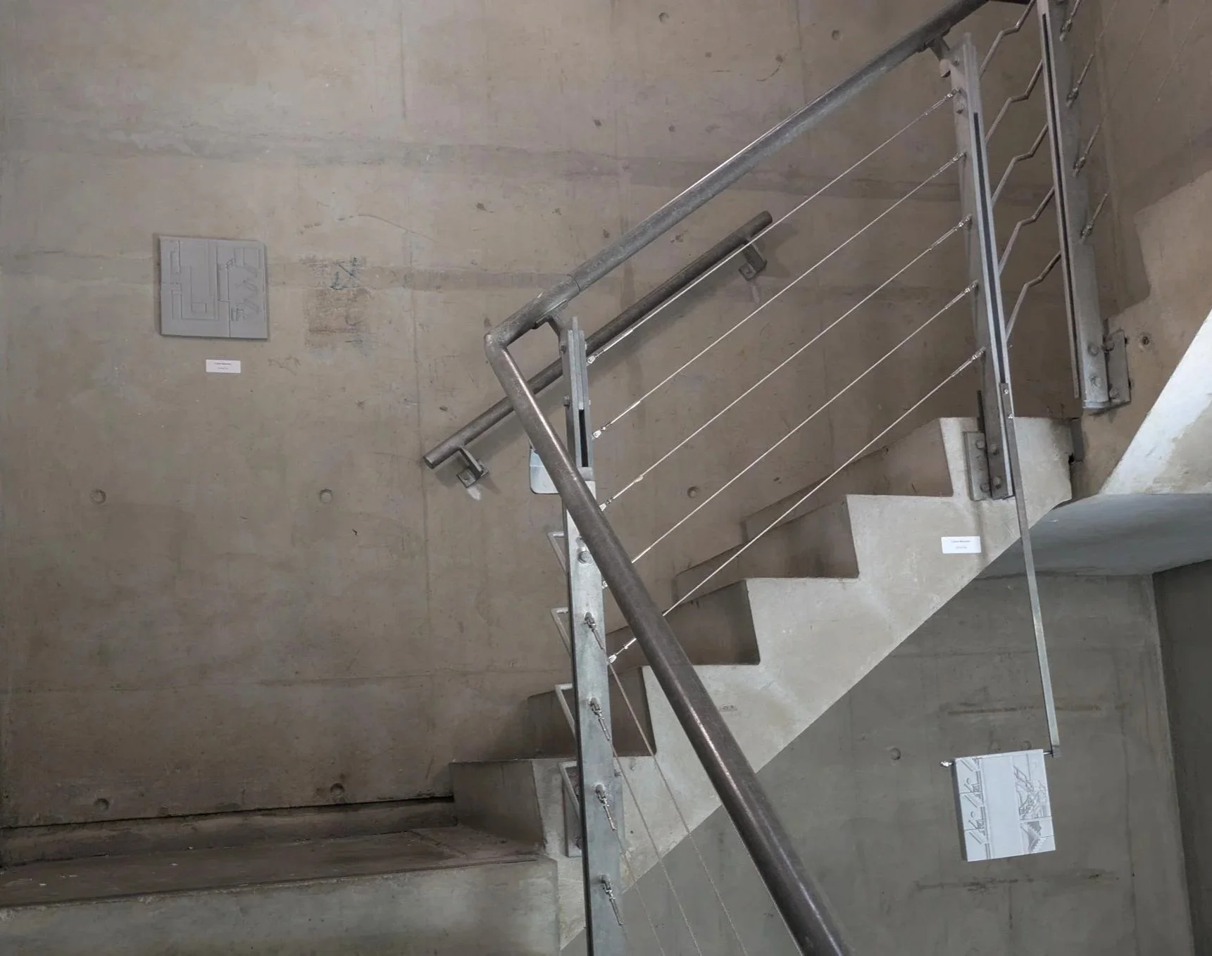 Staircase with concrete steps and metal handrail, seen from above in a minimalistic, modern interior with exposed concrete wall.