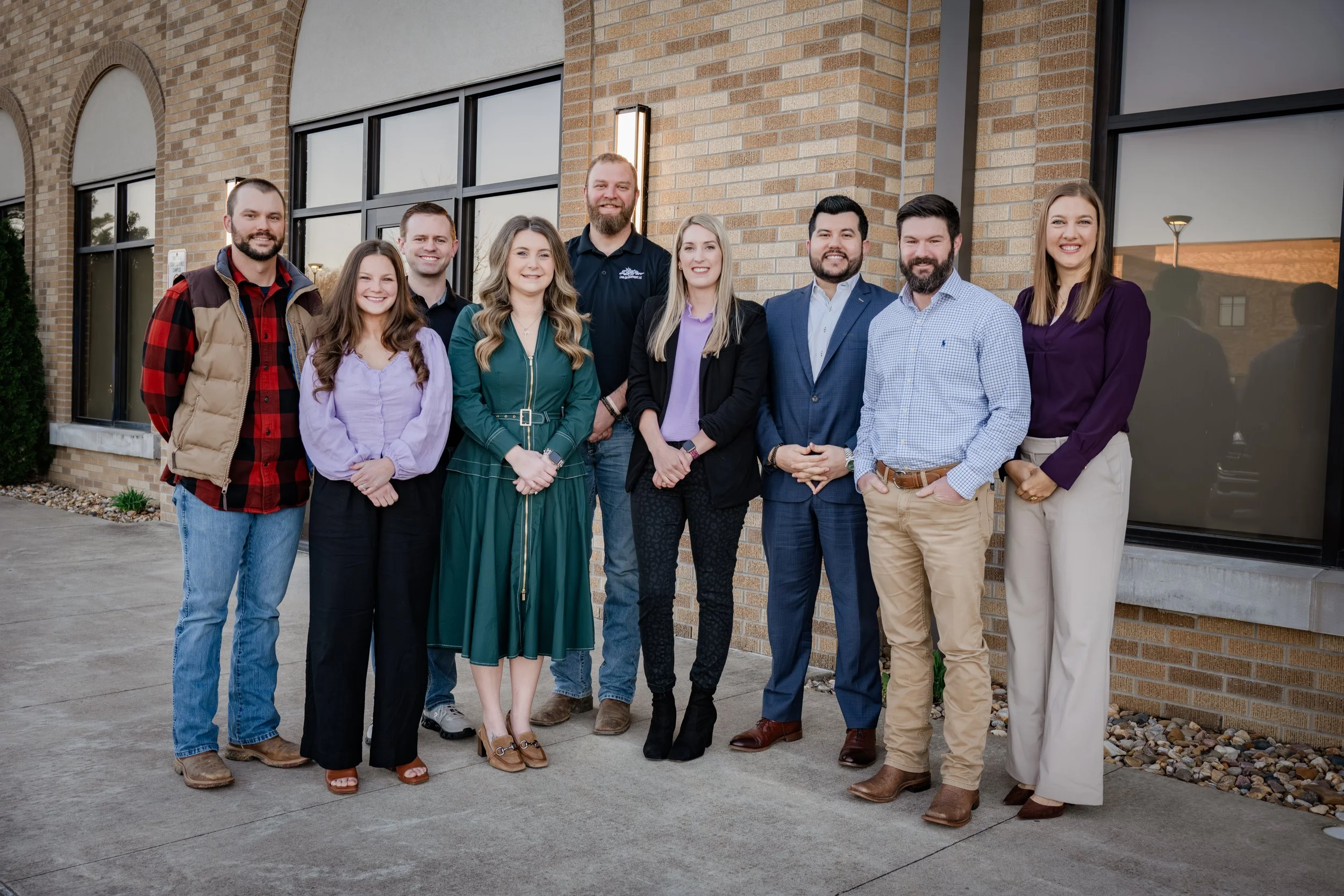 Group of ten people standing outside in front of a brick building, smiling for the photo.