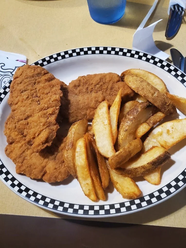 Fried chicken fillets and a serving of French fries on a checkered paper-lined plate.
