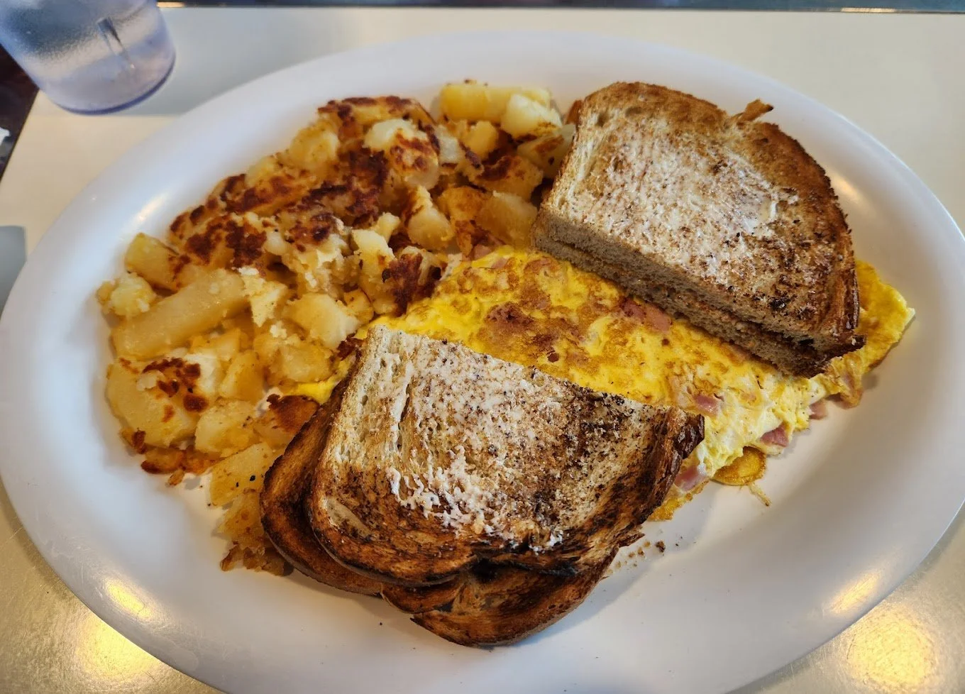 A plate of breakfast food including scrambled eggs with ham, toasted bread, home fries, and a biscuit.