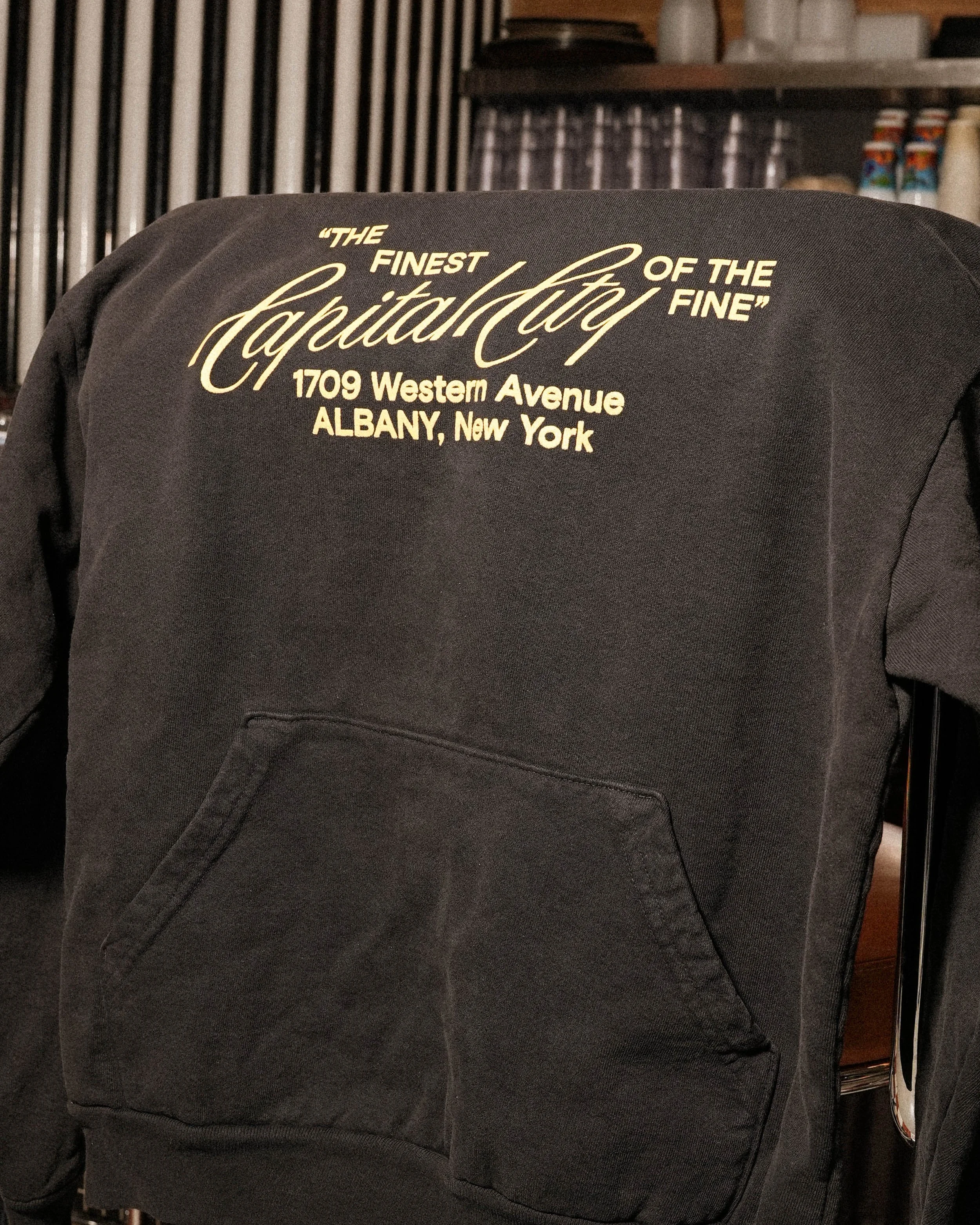 Back of a black hoodie with white cursive and block text reading 'The Finest of the Currency.