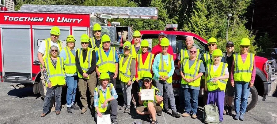 Group of people wearing safety vests and helmets standing in front of a fire truck.