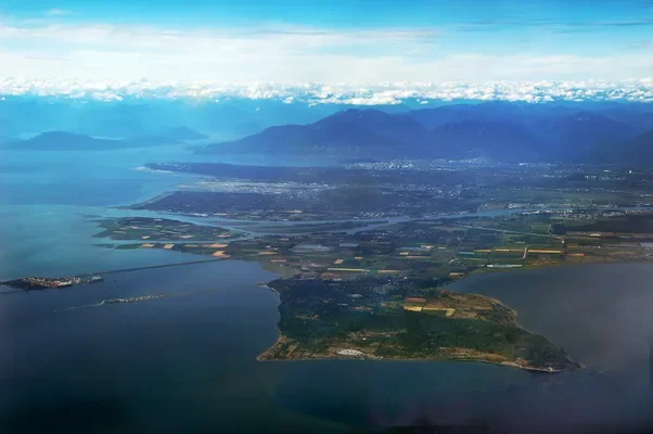 Aerial view of a coastal region with peninsulas, water bodies, farmland, and mountains in the distance.