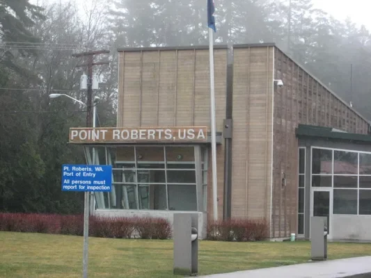 Building with a sign that reads "Point Roberts, USA." A blue sign indicates it is a port of entry, requiring all persons to report for inspection.