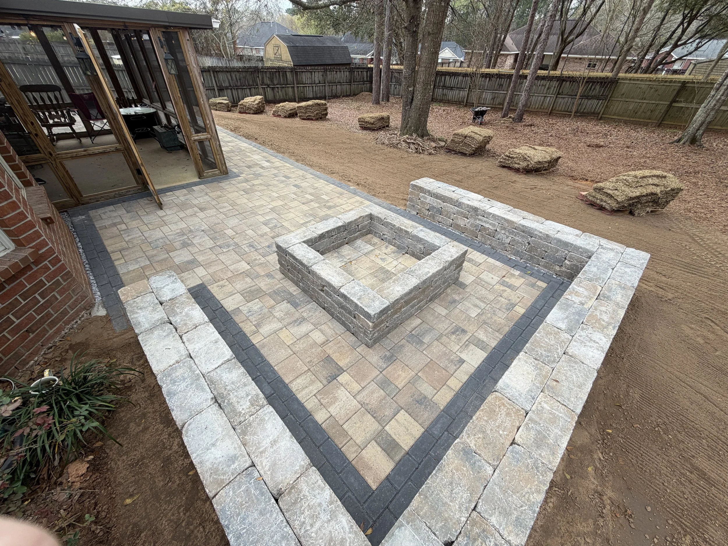 Backyard patio area with brick and stone pavers, a small brick fire pit, built by Noah's Hammer in Mobile, Alabama.