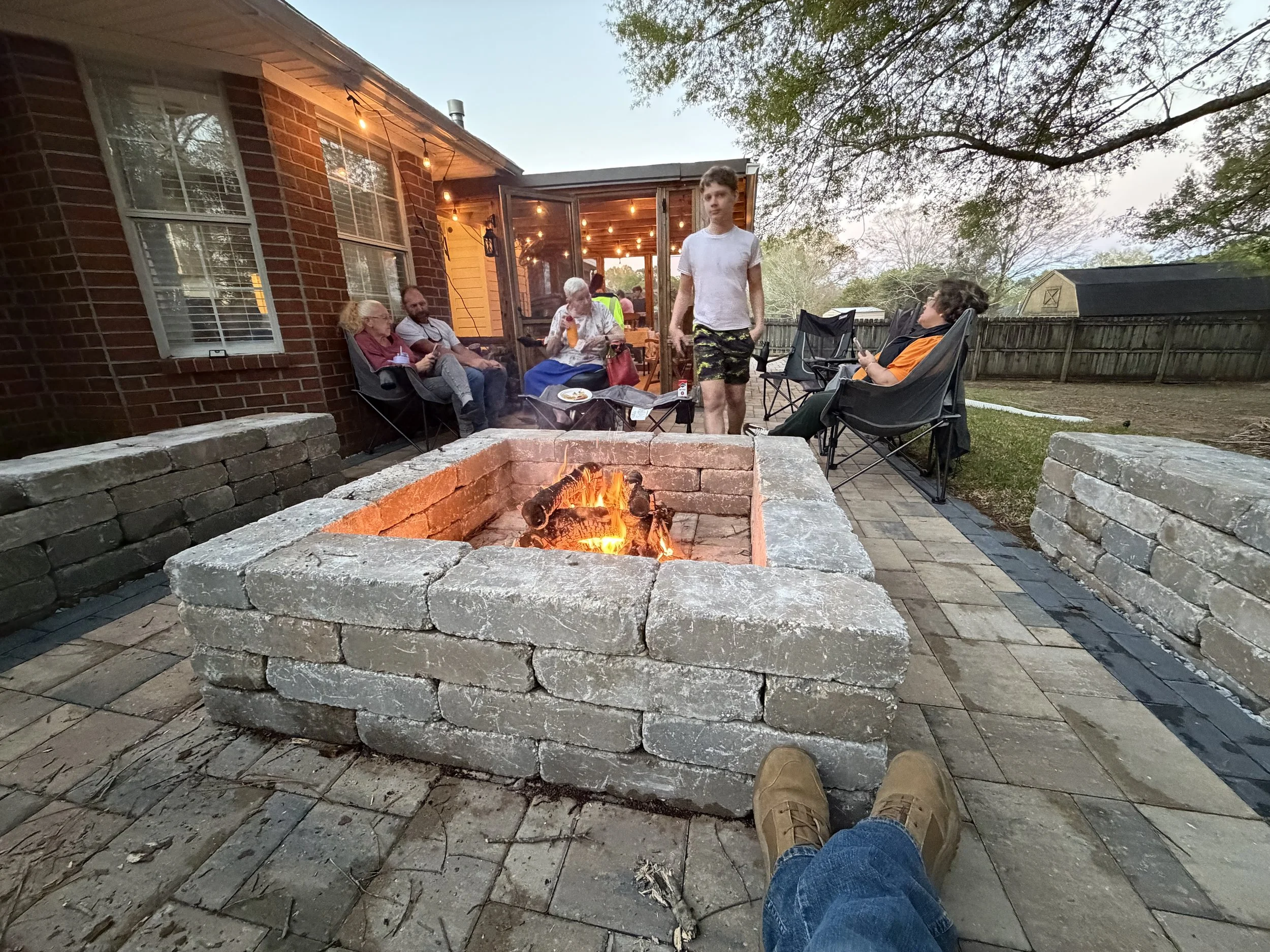 People sitting and standing around a backyard fire pit, built by Noah's Hammer in Mobile Alabama.