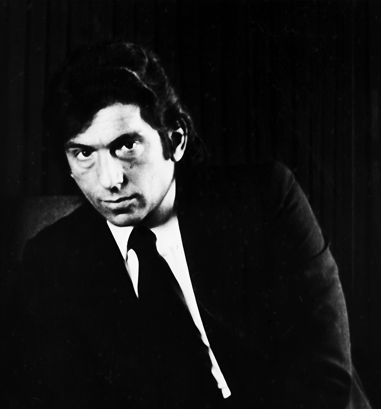 Retrato en blanco y negro de un hombre con cabello oscuro, vestido con saco y corbata, mirando hacia la cámara.
