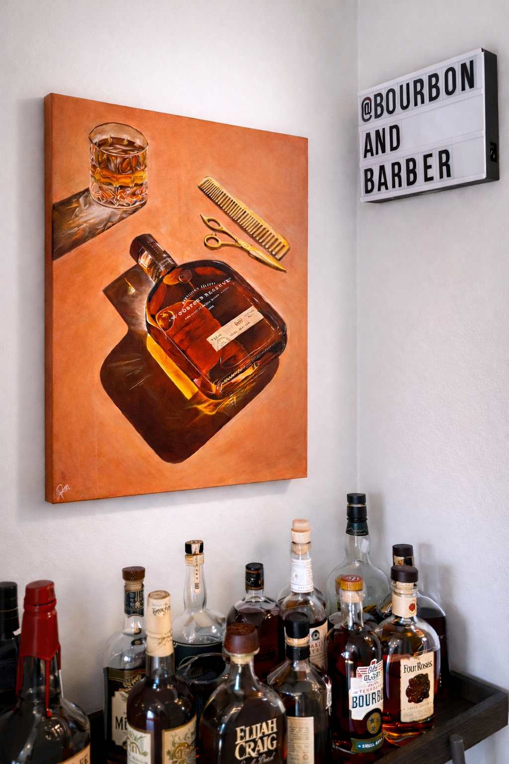A bar corner with a painting of a whiskey bottle, glass, comb, and scissors on the wall; bottles of whiskey on the bar counter; a lightbox sign reads '@BOURBON AND BARBER'.