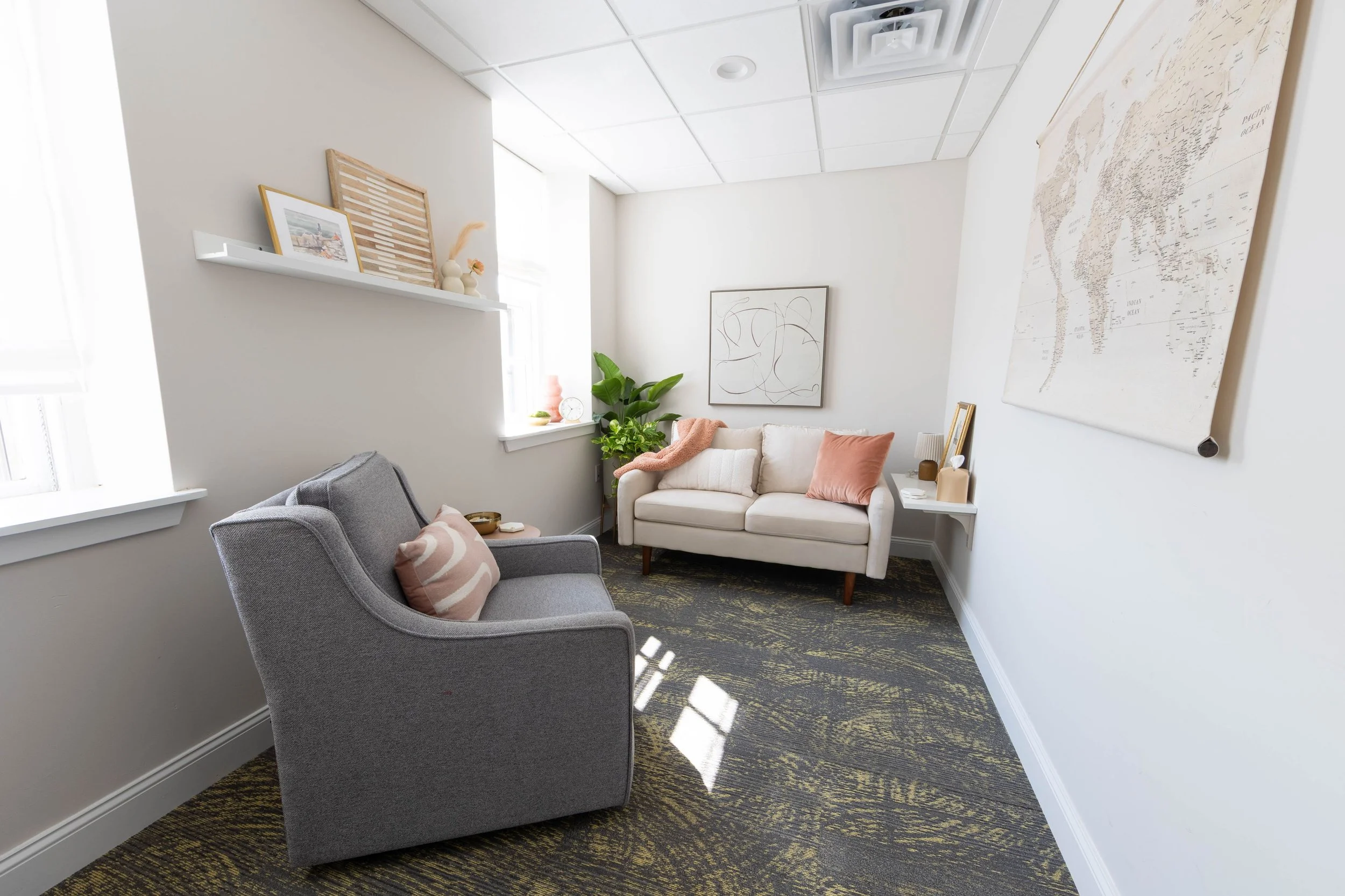 Therapy room with a gray armchair and cream loveseat, natural lighting, abstract art, and green plants at Shelley Snapp Therapy's Doylestown, PA office