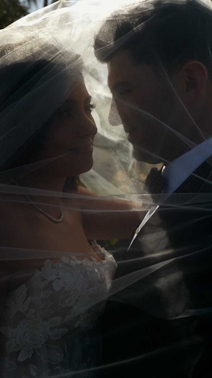 A bride and groom intimate moment under a wedding veil during their wedding.