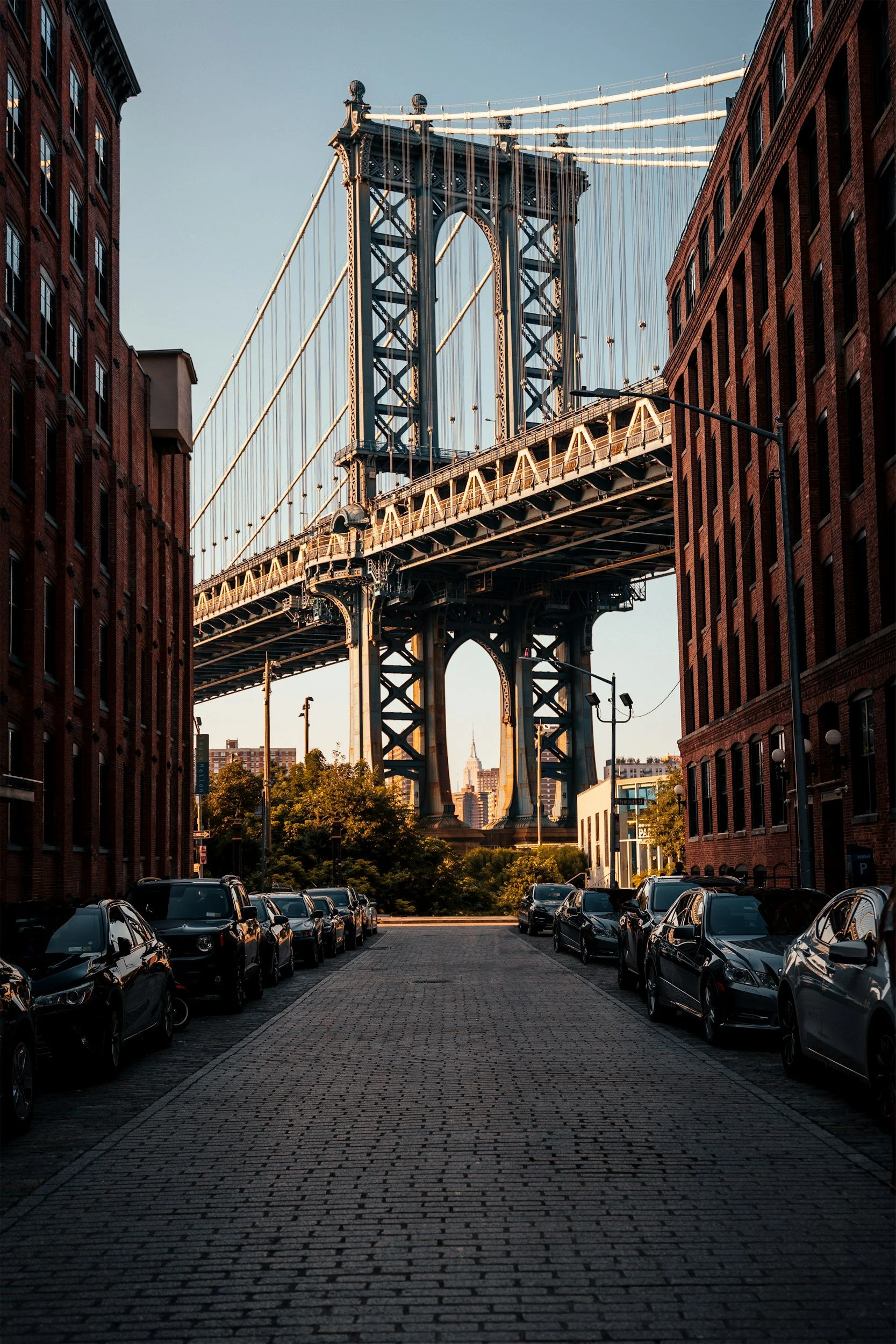 Manhattan Bridge viewed from DUMBO, Brooklyn, framed by brick buildings with the Empire State Building in the distance.