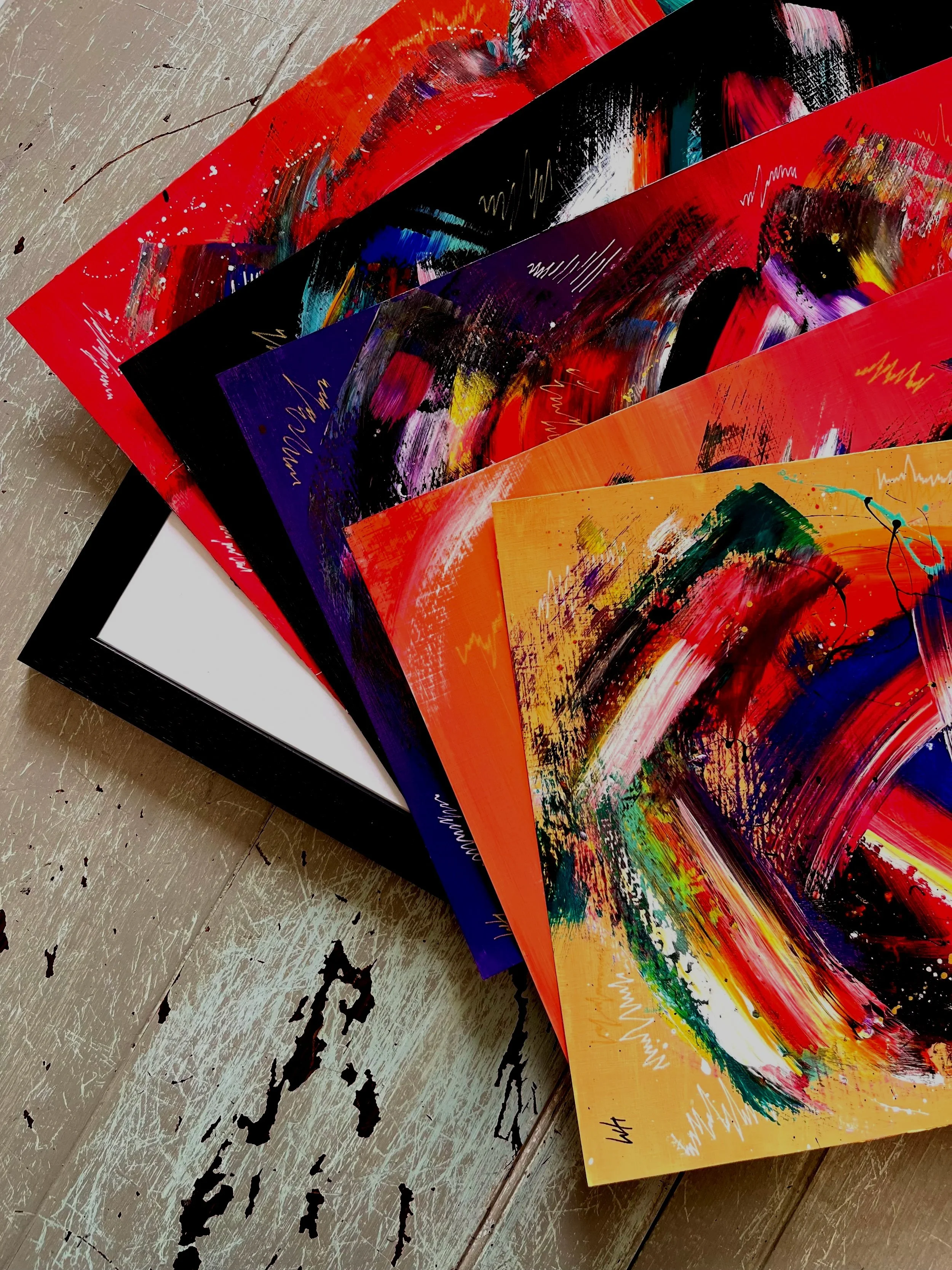 Set of four colorful abstract art prints arranged on a distressed wooden surface.