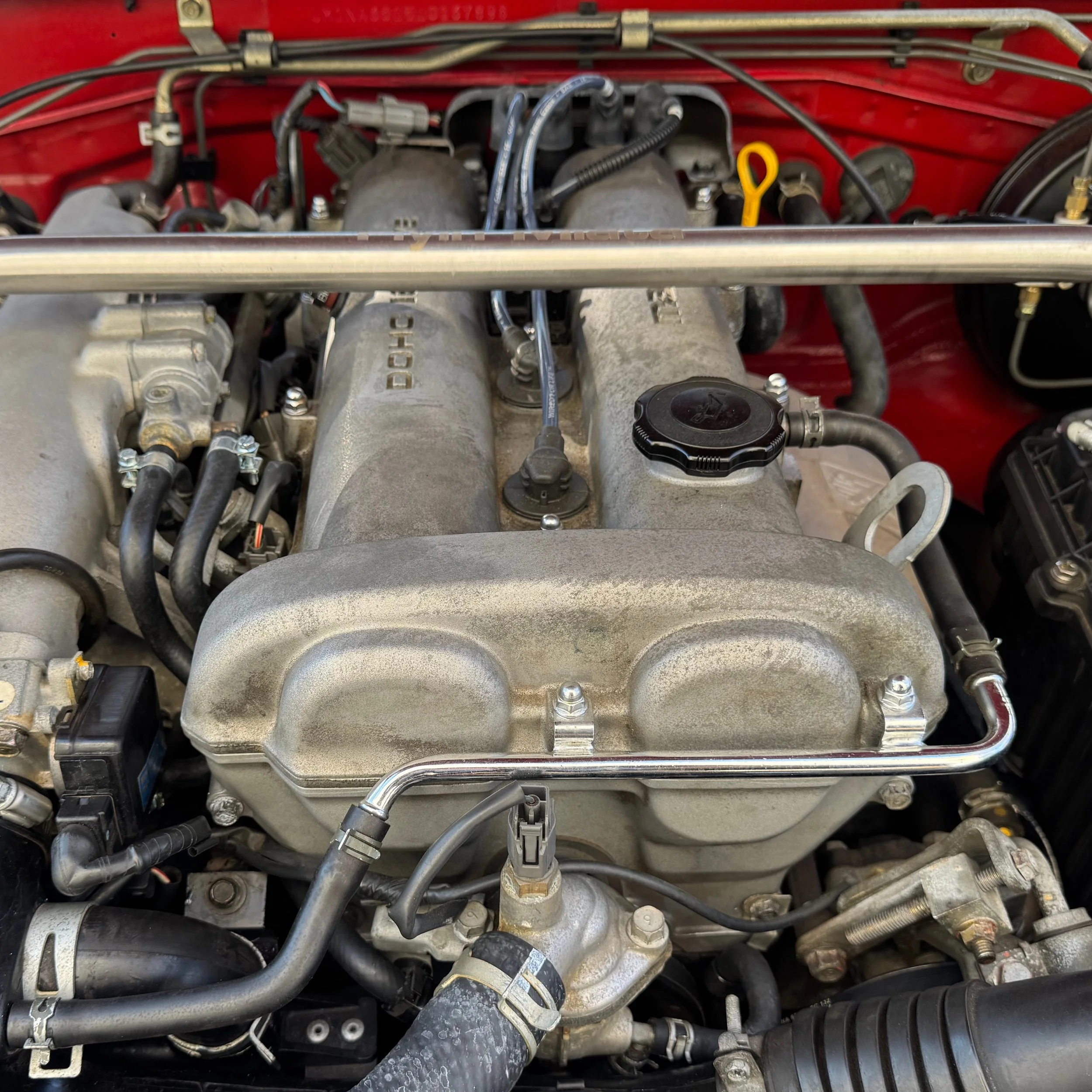 Engine bay of 1990 NA Miata MX-5 with Flyin' Miata shock tower brace. Link leads to NA Miata Maintenance Schedules.