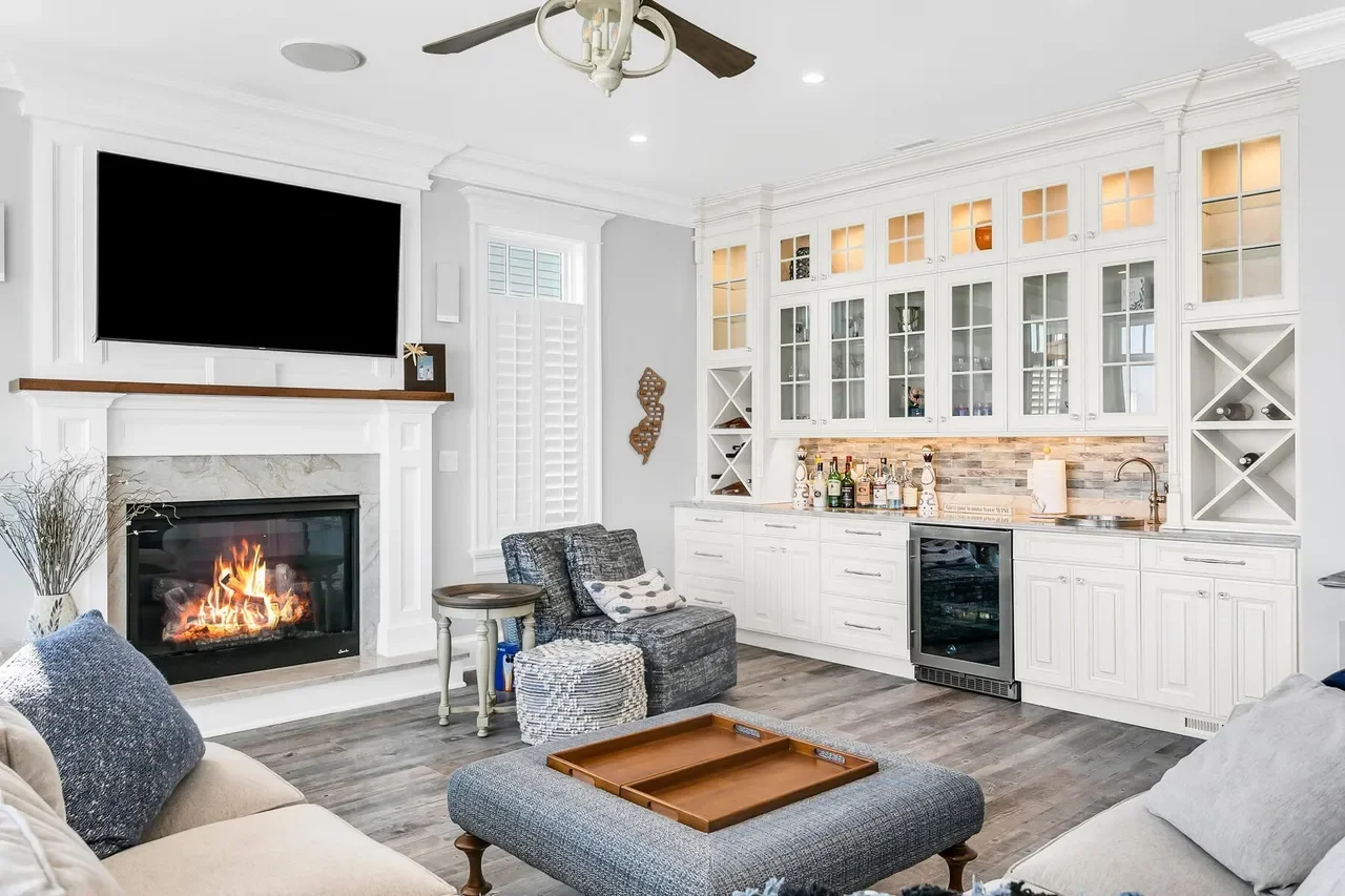 Living room with white built-in bar area, fireplace, large flat-screen TV, and gray furniture.