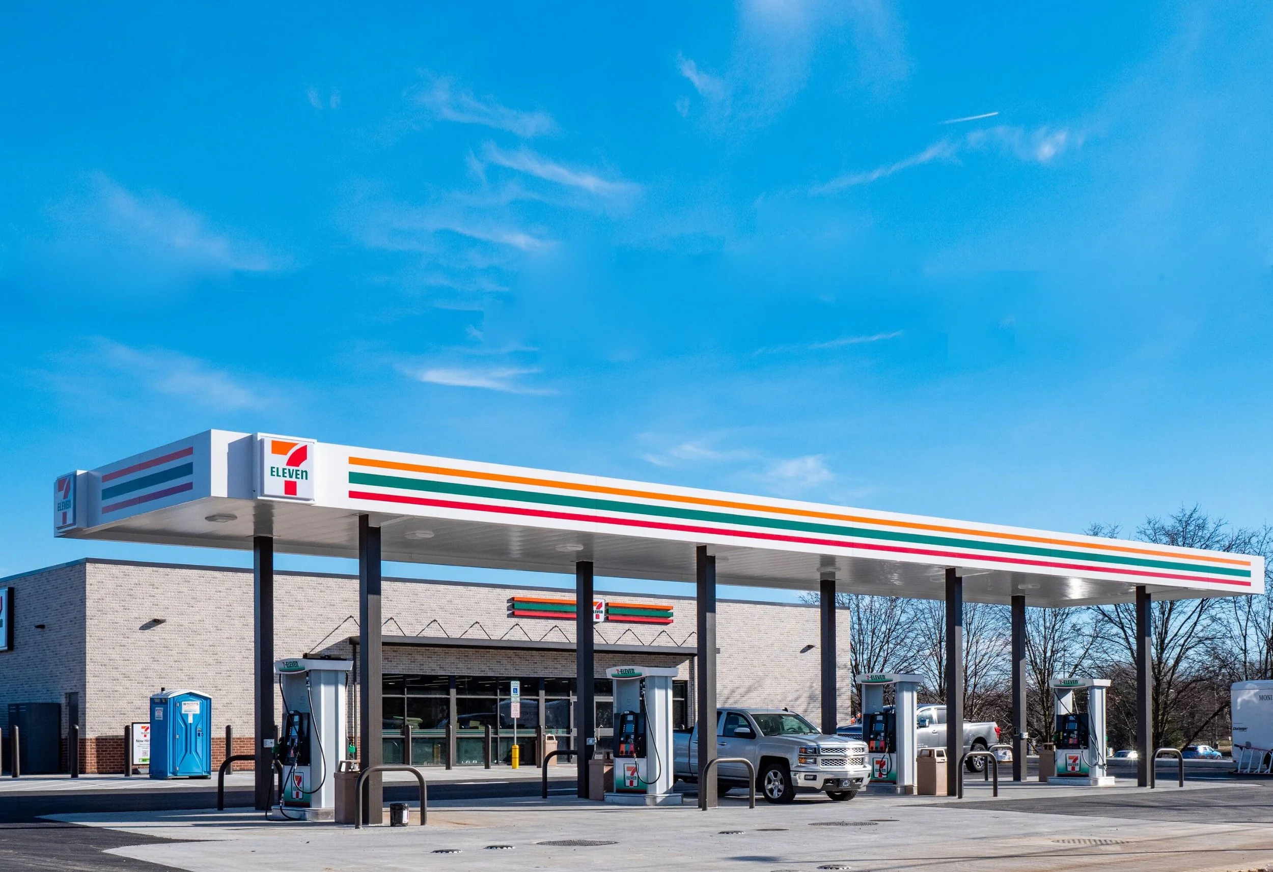 A 7-Eleven convenience store with fuel pumps and cars parked outside on a clear day.