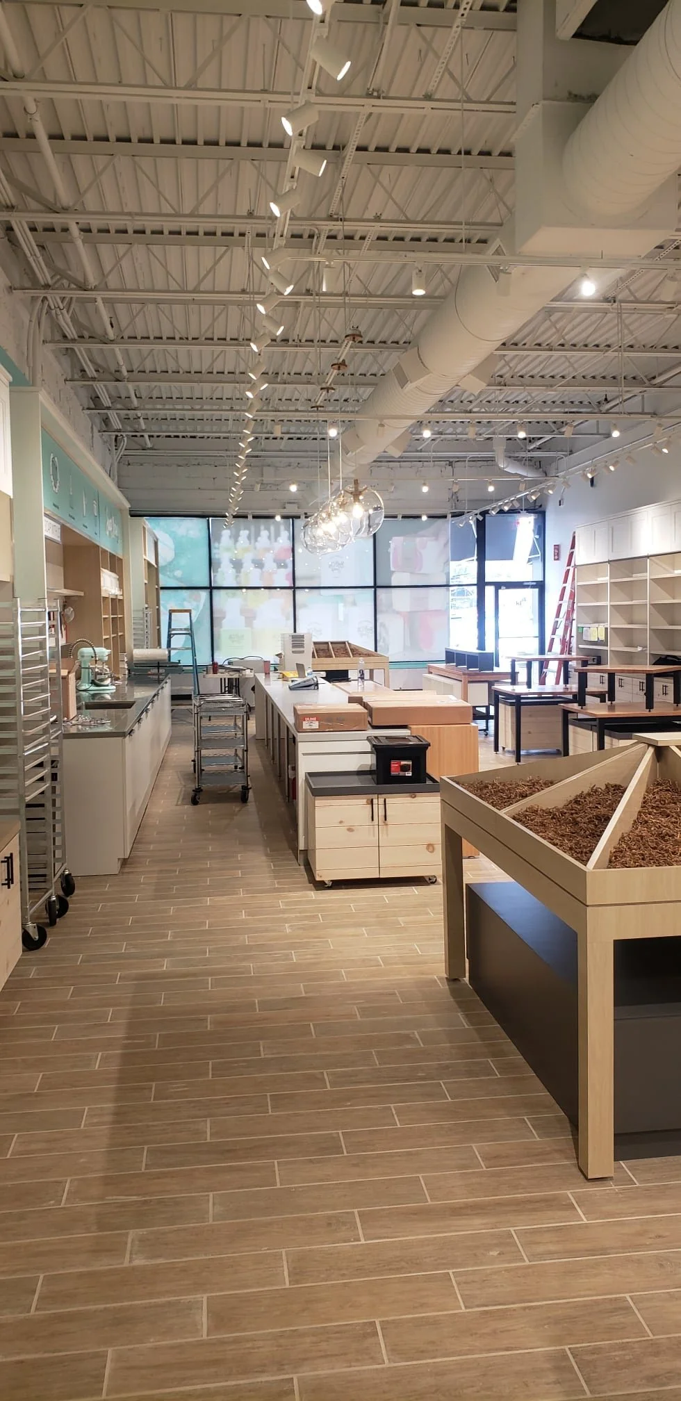 Empty retail store with wooden flooring, cabinetry, shelves, and a ladder, possibly under setup or renovation.